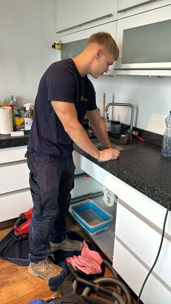 Monteur controleert en ontstopt een keukenafvoer onder de gootsteen - praktijkbeeld