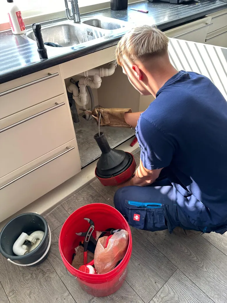 Monteur controleert en ontstopt een keukenafvoer onder de gootsteen - praktijkbeeld